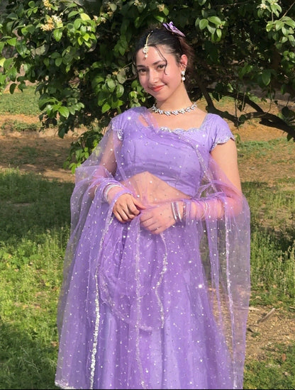 Woman in a purple aishwarya lehenga outfit standing outdoors with greenery in the background